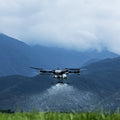 DJI T100 flying low over a field with mountains in the background