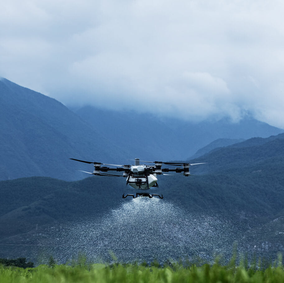 DJI T100 flying low over a field with mountains in the background