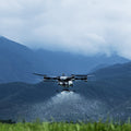 DJI T100 flying low over a field with mountains in the background